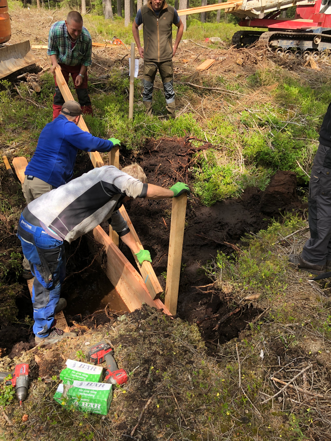 Arbeiter setzen die Holzspundwand in den Graben ein.